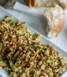 A rectangular white platter with a couscous and Brussels sprouts salad and a loaf of bread with a piece torn off of it next to the platter.
