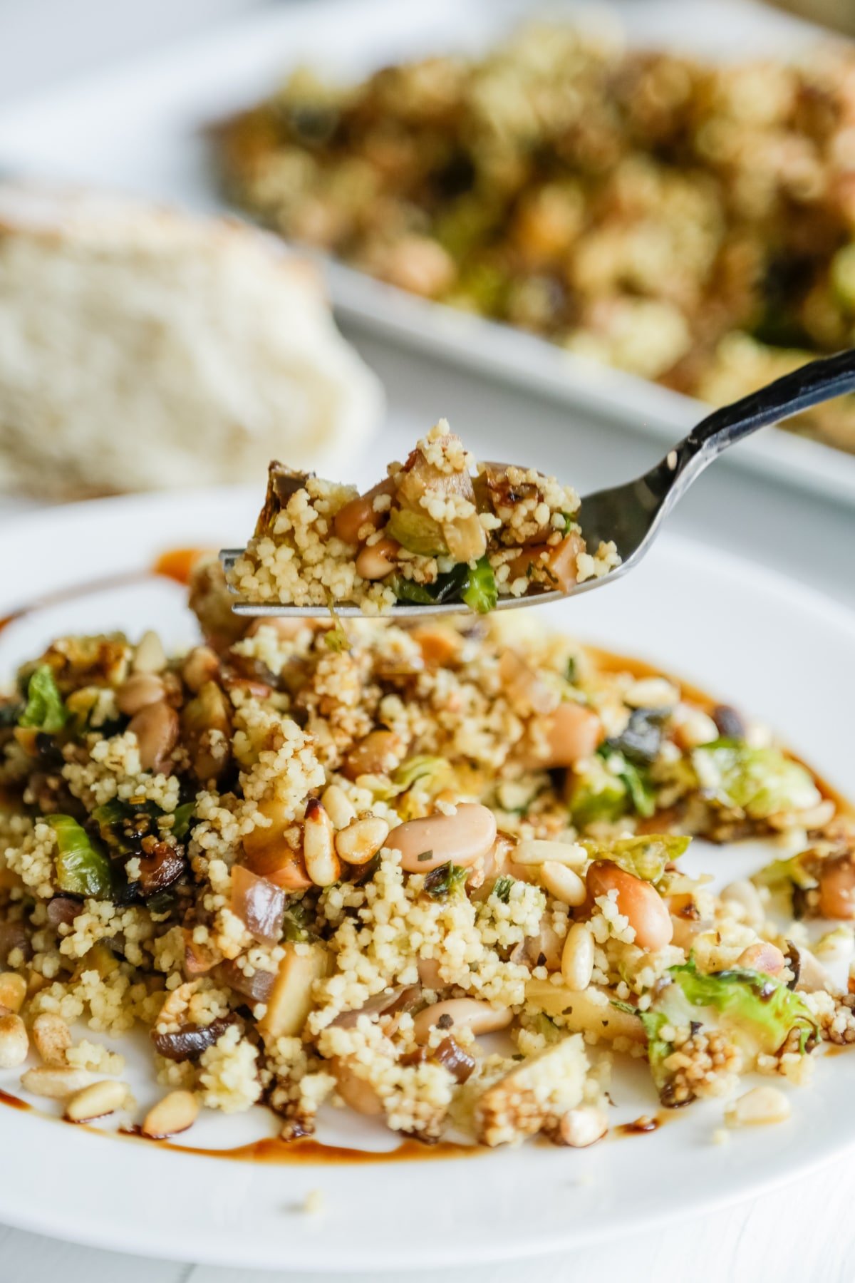 A fork with warm couscous and Brussels sprouts salad being held over a white plate of the salad. 