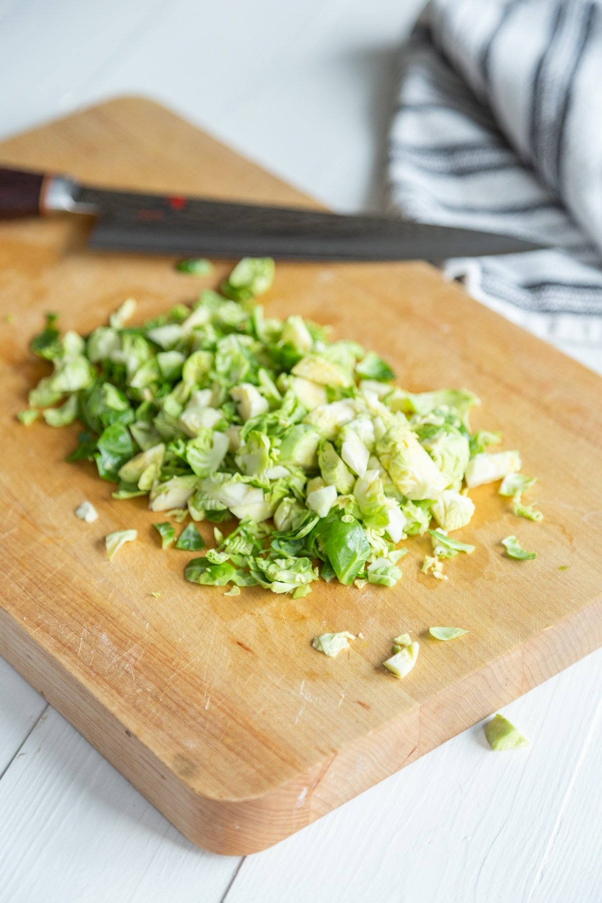 A wood cutting board with a knife and chopped Brussels sprouts.