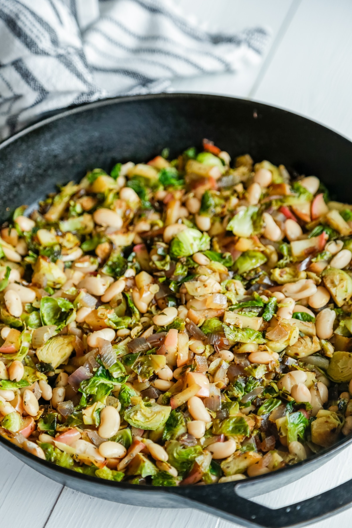 An iron skillet with Brussels sprouts, apple, and cannellini beans. 