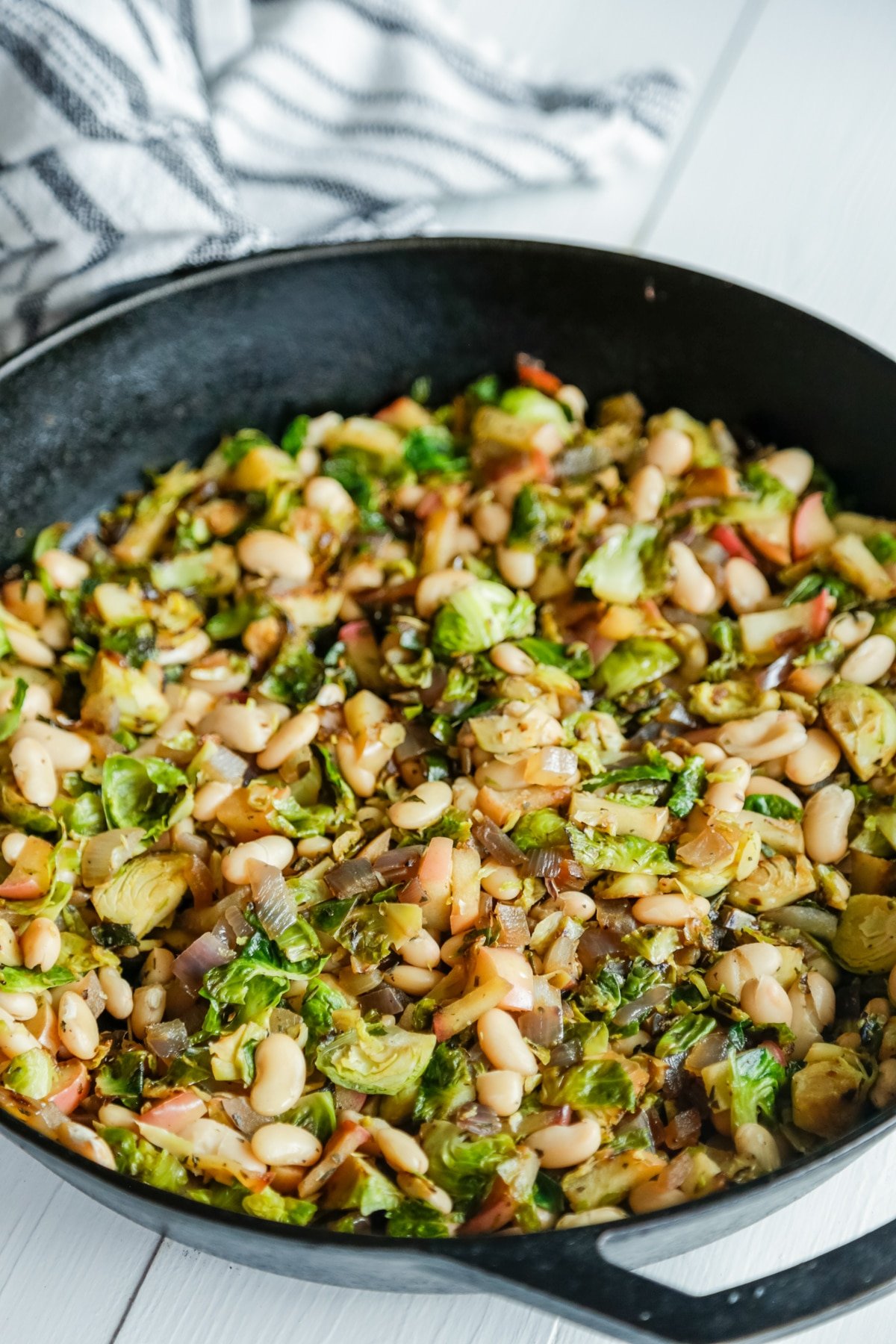 An iron skillet with Brussels sprouts, apple, and cannellini beans. 