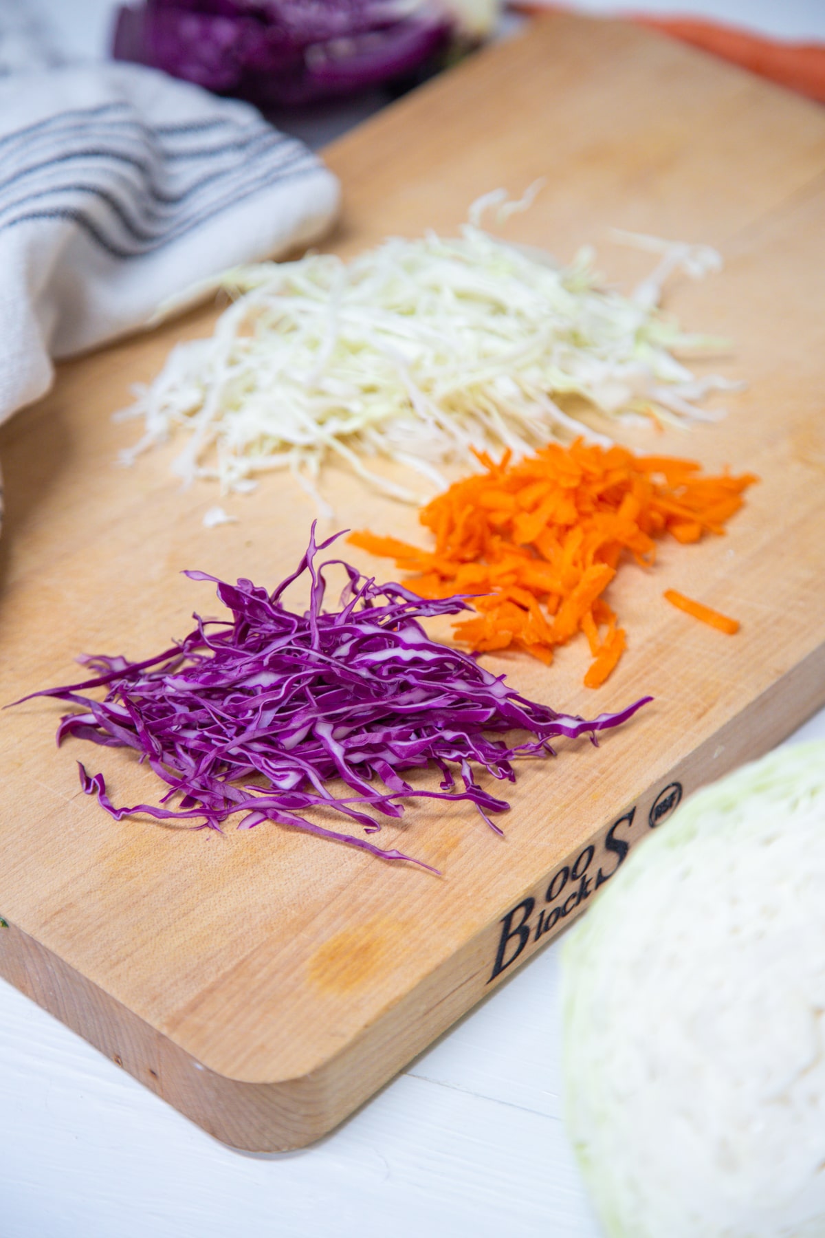 A wooden cutting board with shredded red and green cabbage and grated orange carrots. 