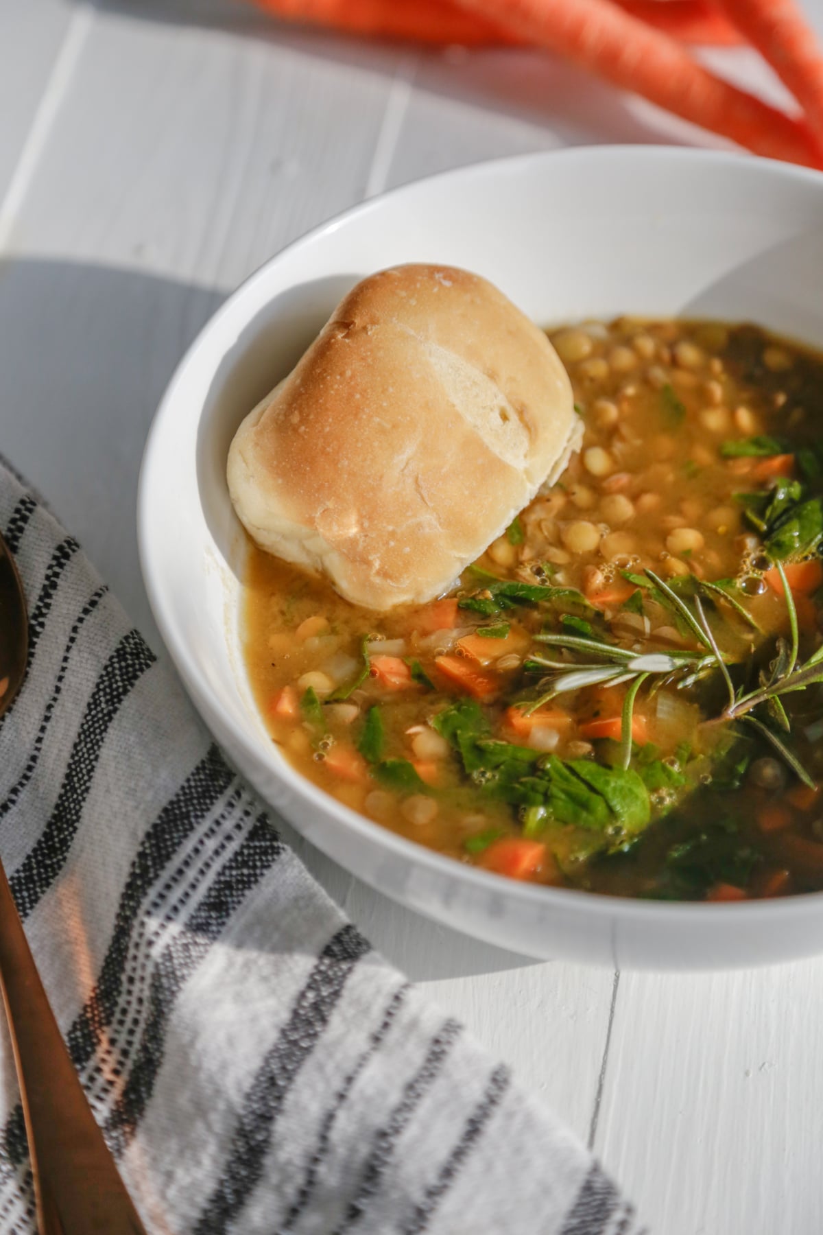 An overhead shot of lentil and carrot soup with a piece of bread in the bowl and carrots in the background.