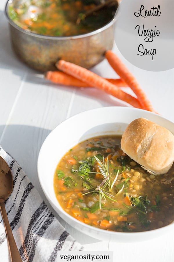 A Pinterest pin for veggie lentil soup with a picture of a white bowl of soup with a bread roll in the soup and a stack of carrots and the pot of soup in the background.