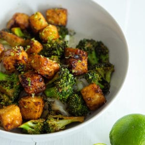 A white bowl with cubed fried tofu and broccoli over rice with a ½ of a lime, squeezed.