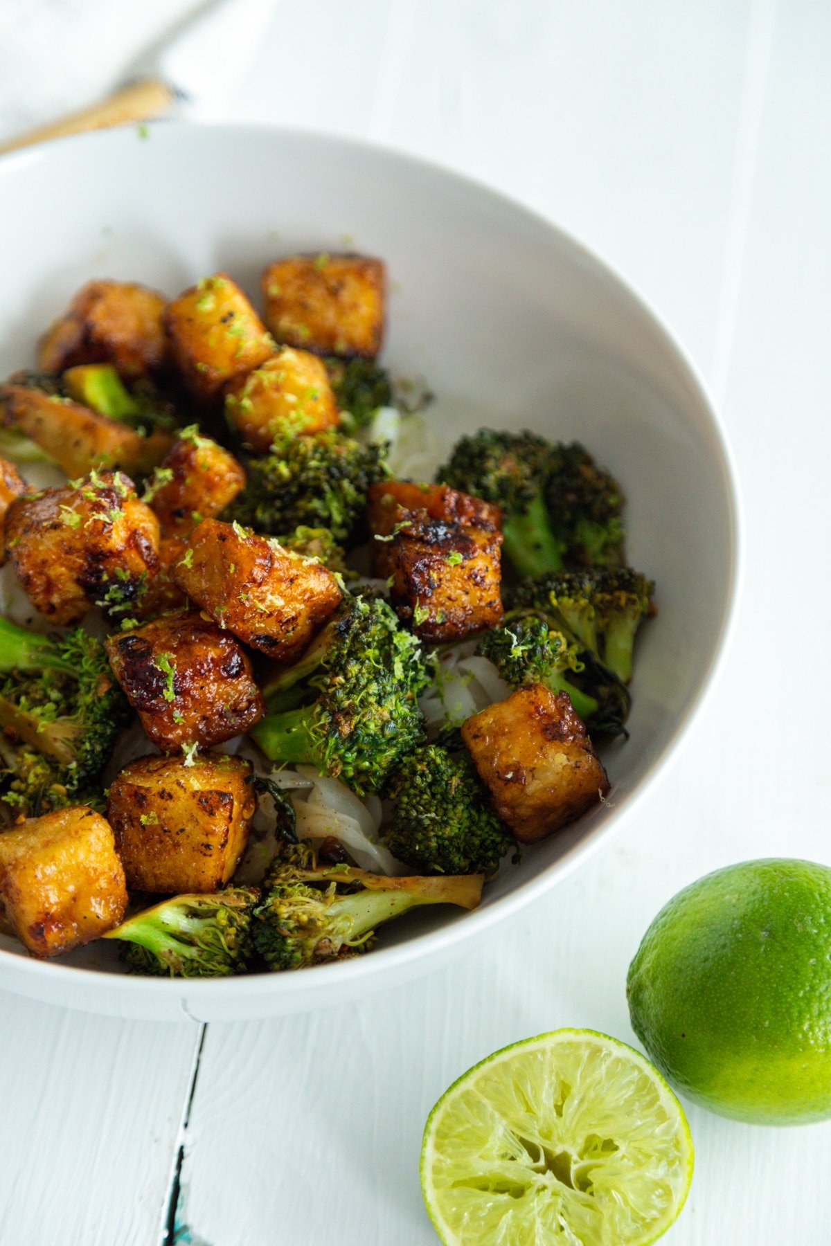 A white bowl with cubed fried tofu and broccoli over rice with a ½ of a lime, squeezed.