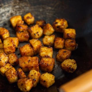 A close up picture of cubed fried tofu in a wok with wooden handles.