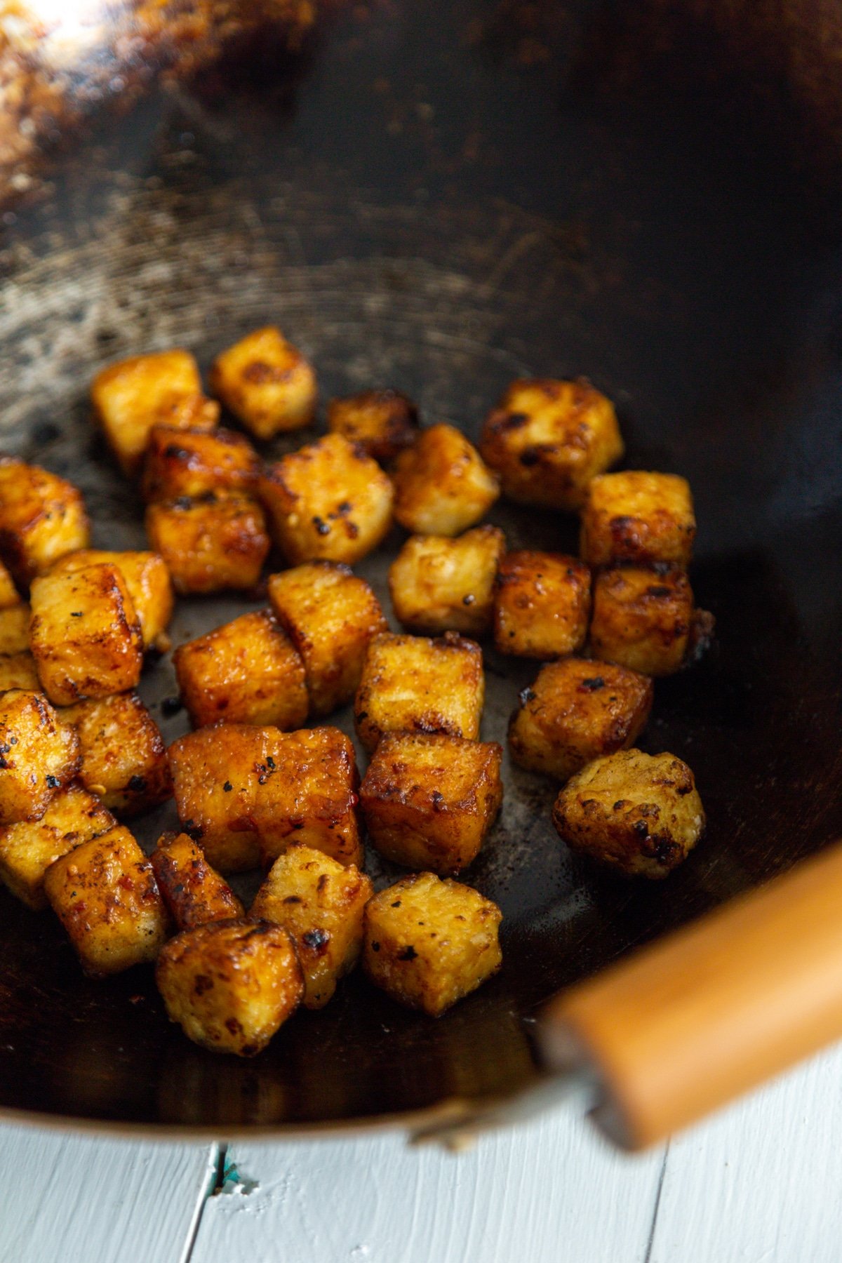 A close up picture of cubed fried tofu in a wok with wooden handles.