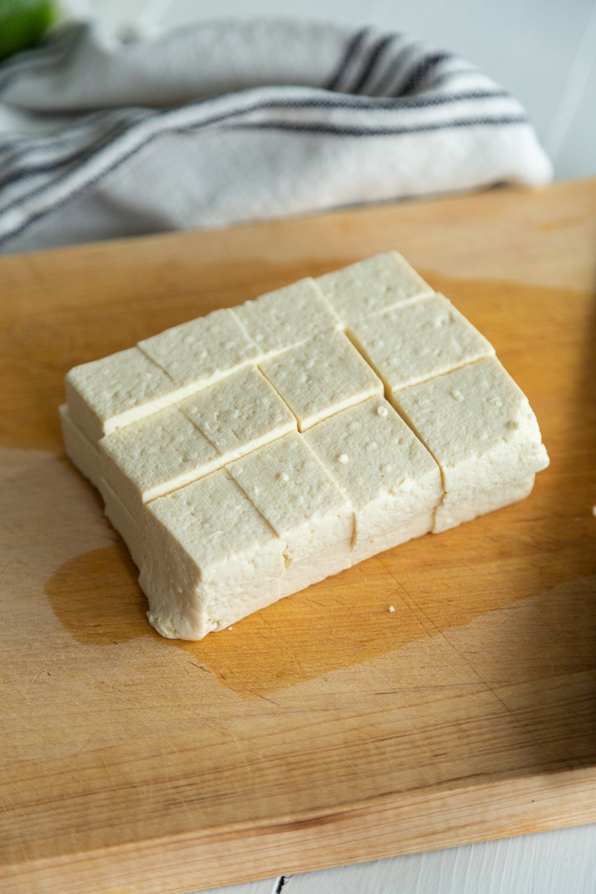 A square piece of tofu cut into cubes on a wooden board.