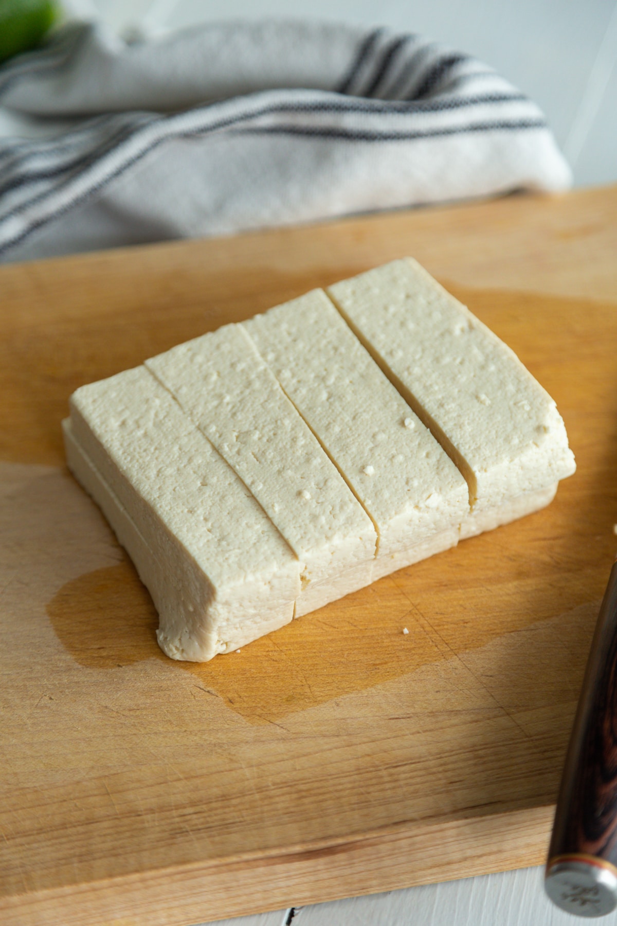 A square piece of tofu cut into strips on a wooden board.