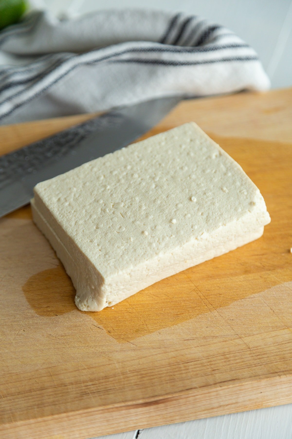 A square piece of tofu cut in half on a wooden board.