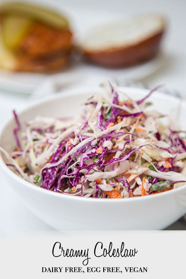A Pinterest pin for creamy vegan coleslaw with a picture of the slaw in a white bowl with bread in the background.