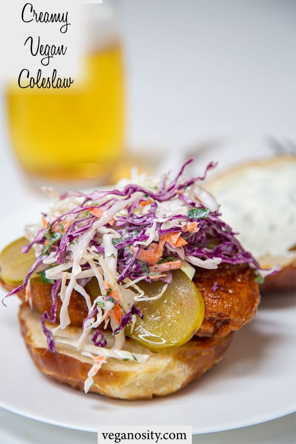 A PInterest pin for creamy vegan coleslaw with a picture of the slaw on top of a fried chicken sandwich with a glass of beer behind it.