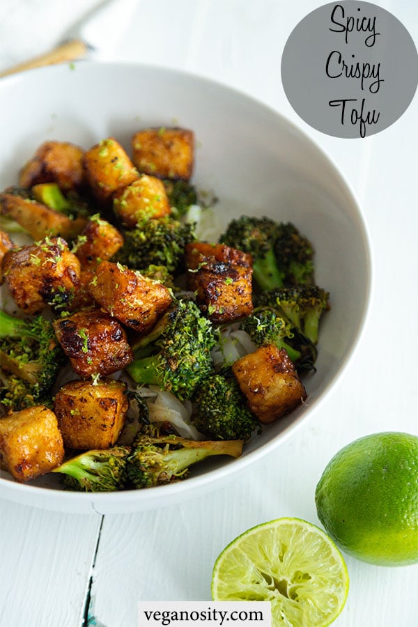 A Pinterest pin for spicy and crispy tofu with a picture of a white bowl with the tofu, broccoli, and rice and 2 halves of a lime next to the bowl.