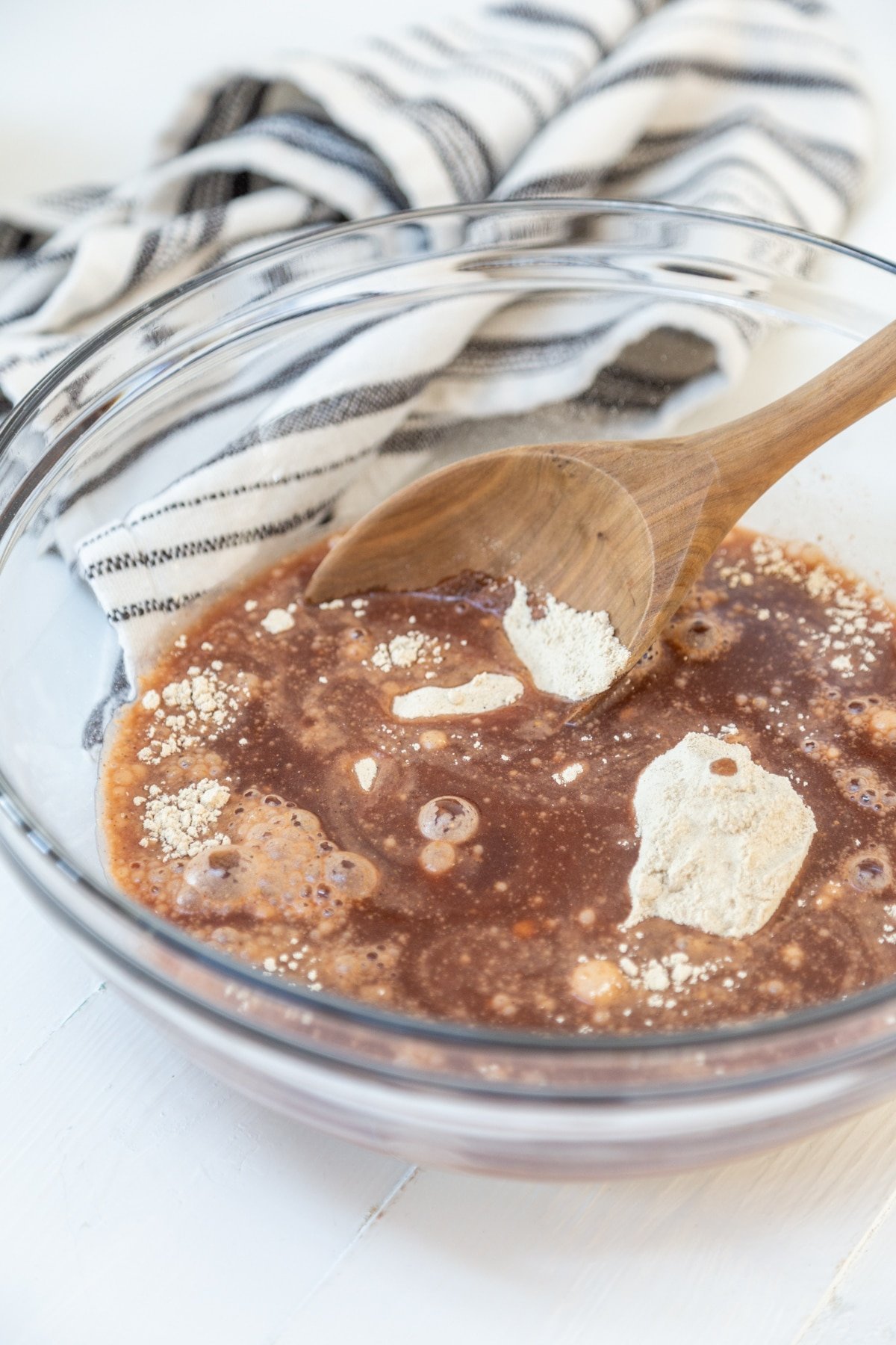 A glass bowl with a wooden spoon stirring spices and flour together.