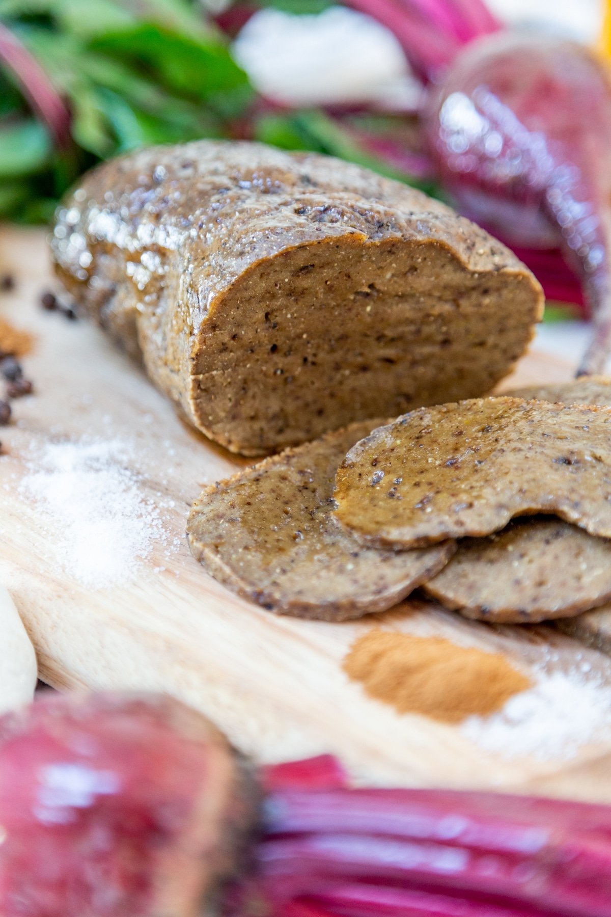 A sliced roast on a wooden board surrounded by beets and spices.