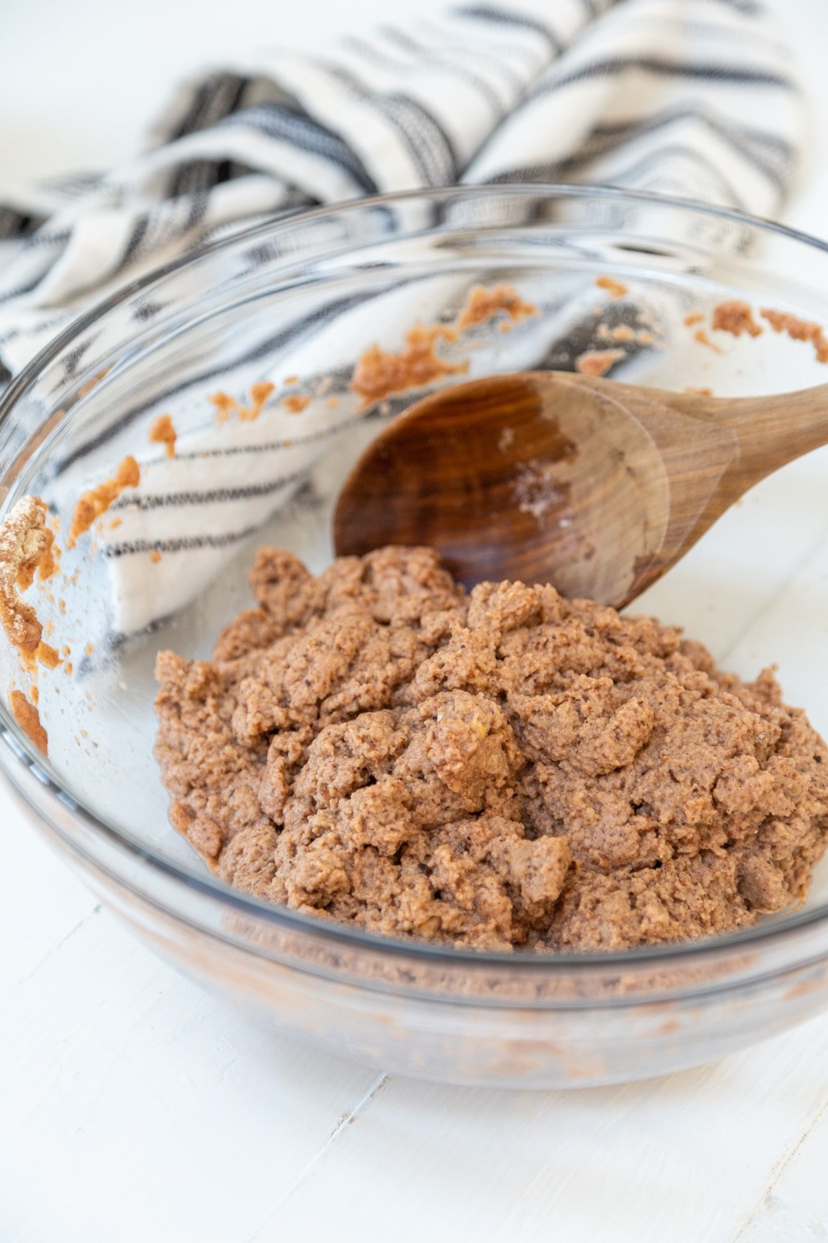 Brown dough in a glass bowl with a wooden spoon.