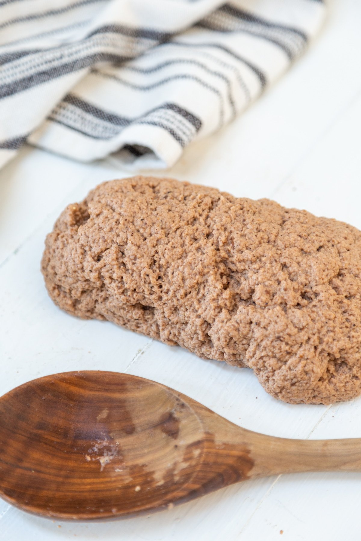 A log of brown dough with a wooden spoon next to it.