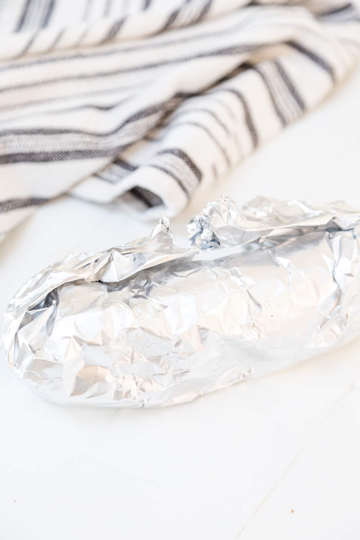 Aluminum foil wrapped around a log of dough with a black and white striped towel next to it.