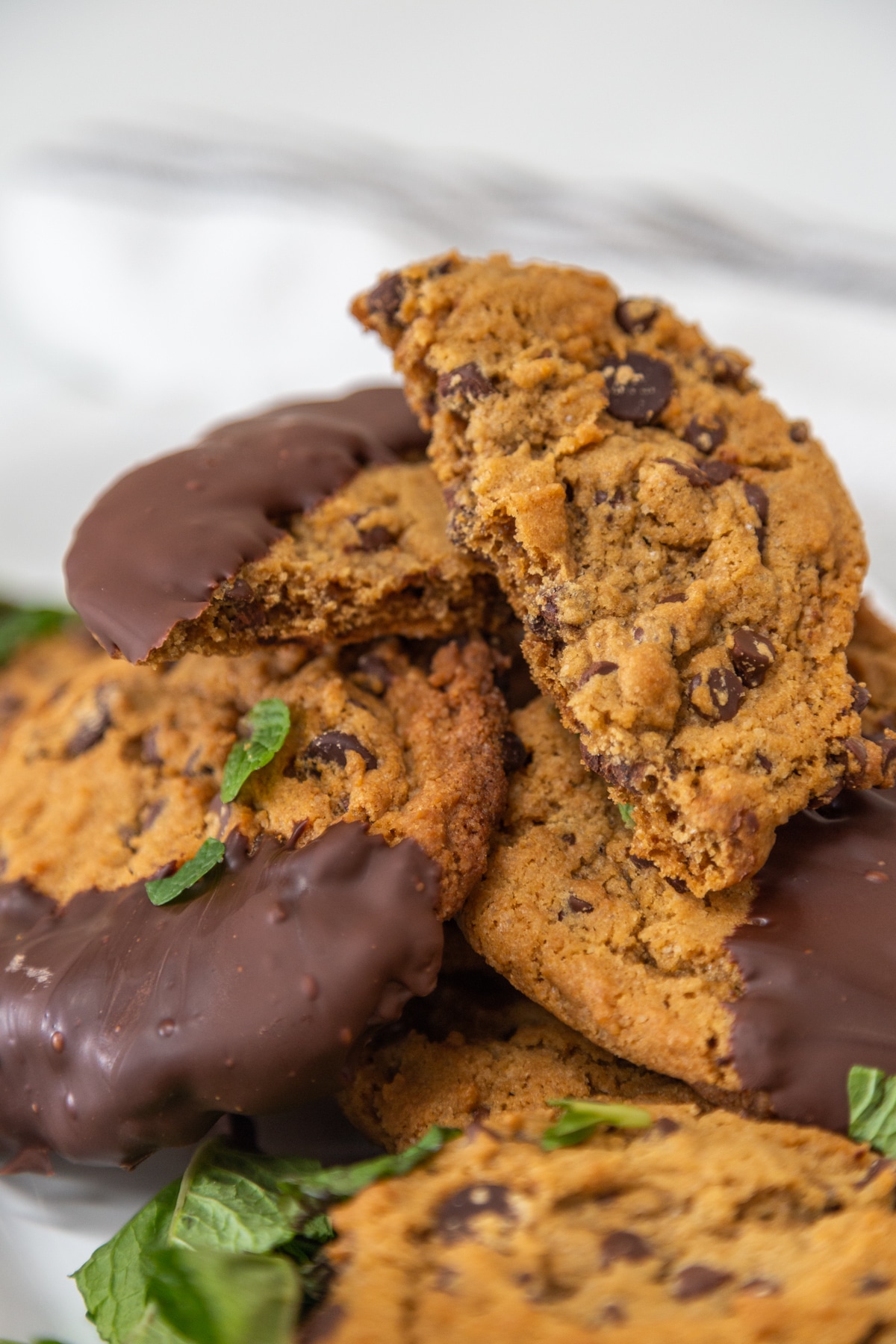 A pile of chocolate dipped cookies with mint leaves on a white platter.