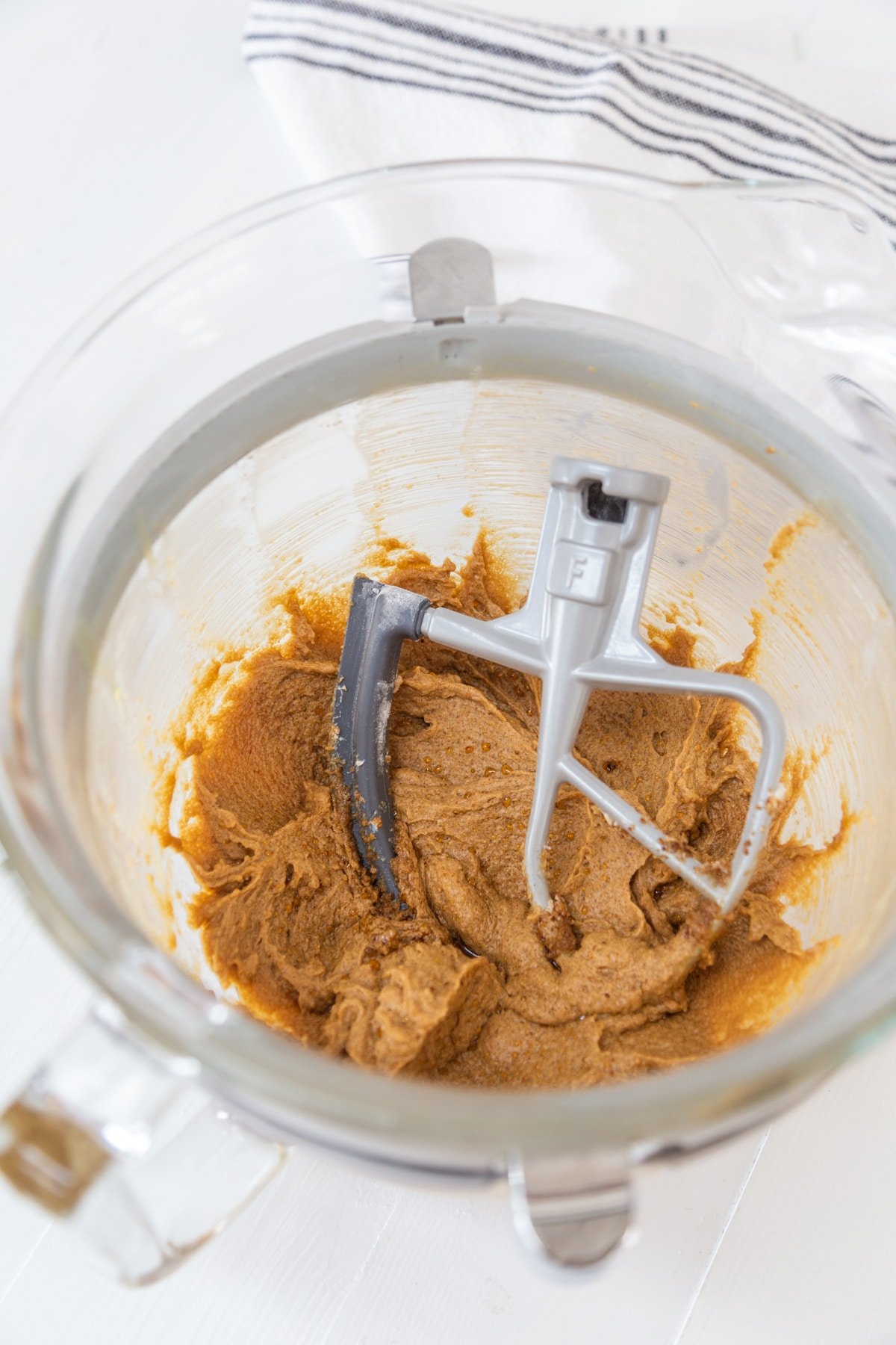 A glass mixing bowl with a paddle attachment and beaten butter and sugar.