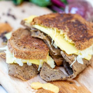 A Reuben sandwich on a wooden board with corned beef and sauerkraut falling out of the sides.