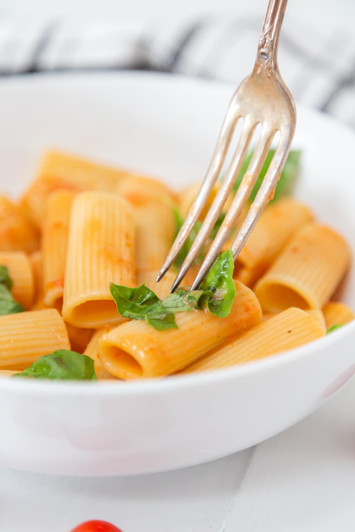 A silver fork piercing a piece of rigatoni with a creamy tomato sauce.