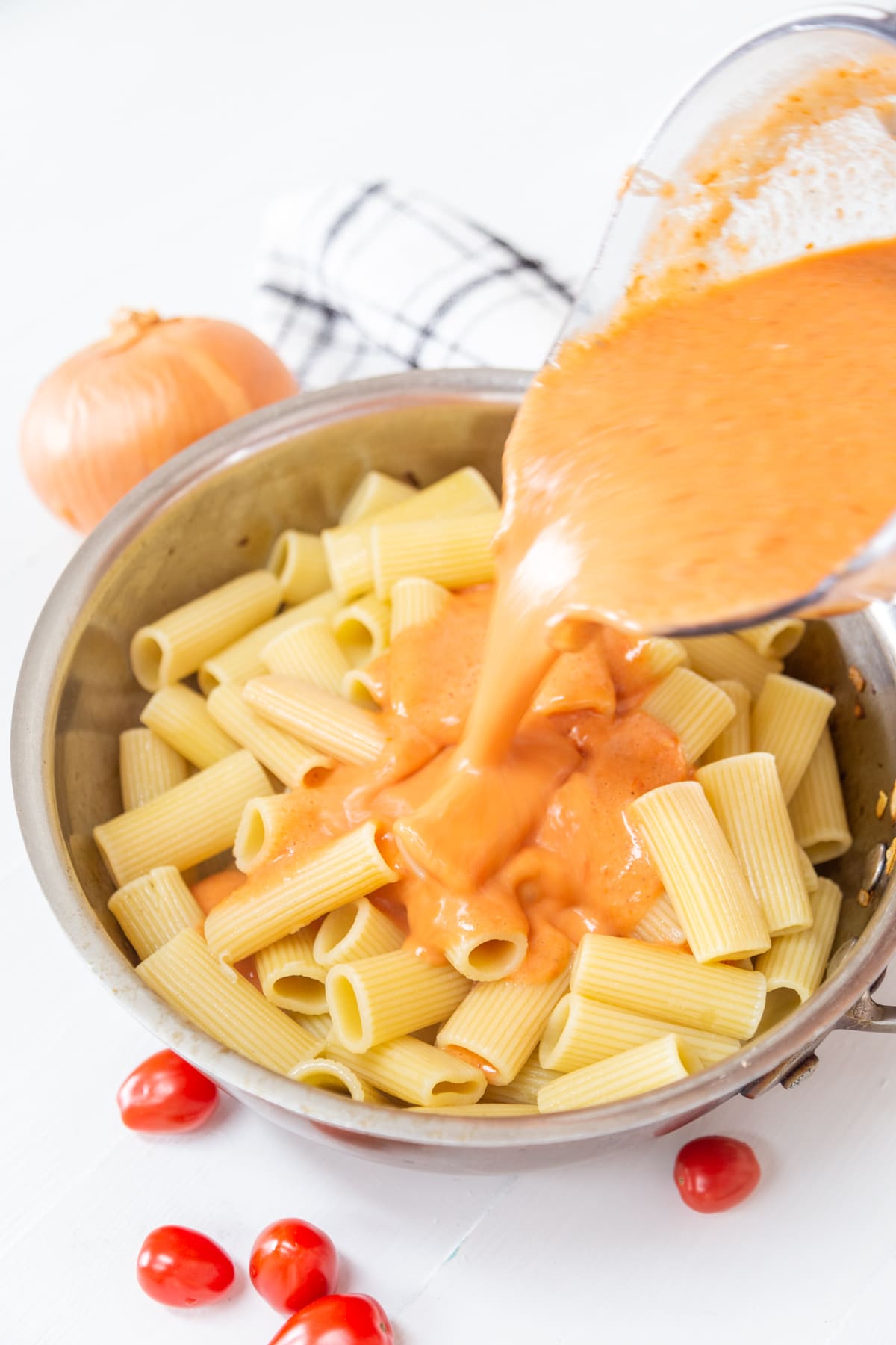 A pan with rigatoni and a pitcher of vodka sauce being poured over the pasta.