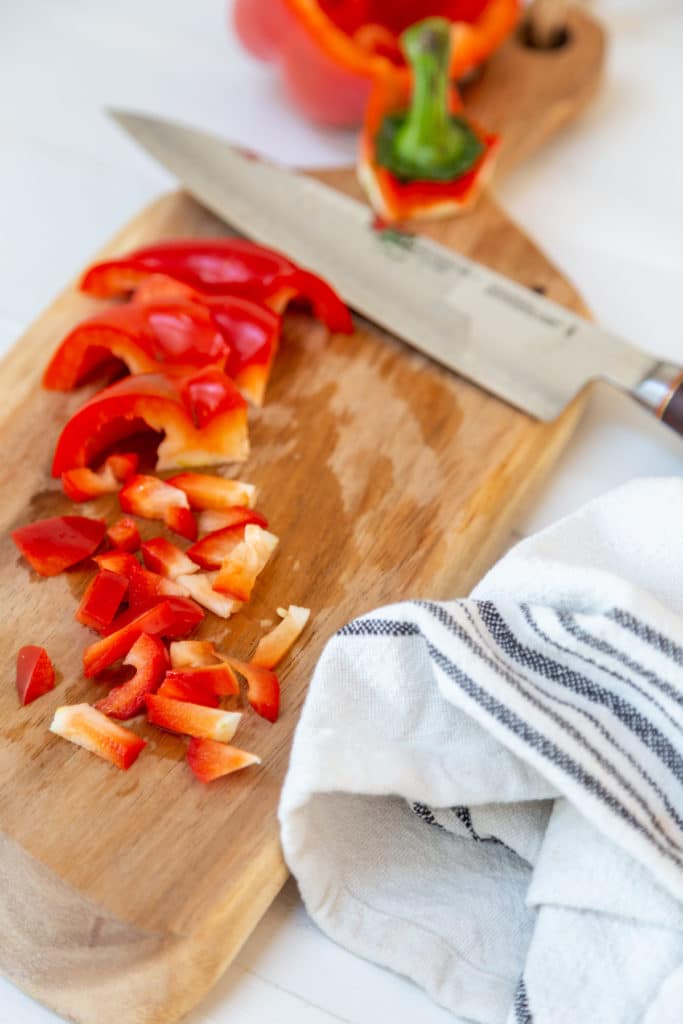 Diced red bell pepper on a wood cutting board with a chef's knife.