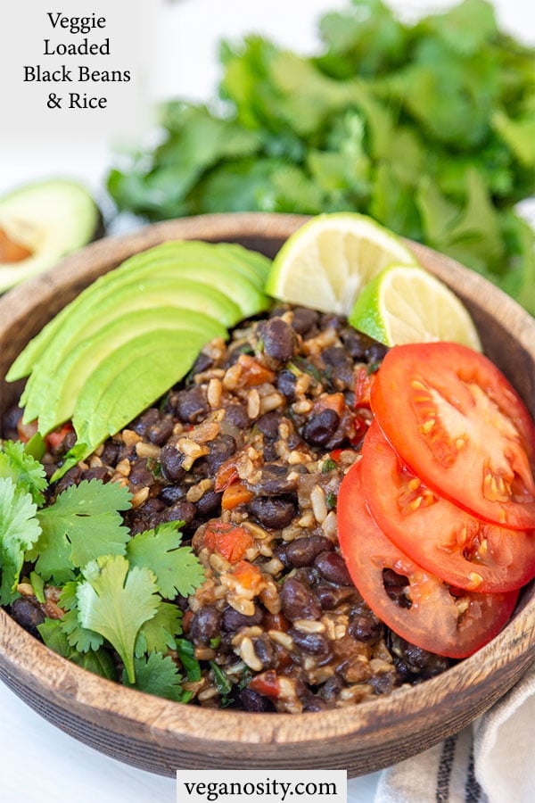 A Pinterest pin for black beans and rice with a picture of the rice and beans with avocado and tomato slices in a wooden bowl.