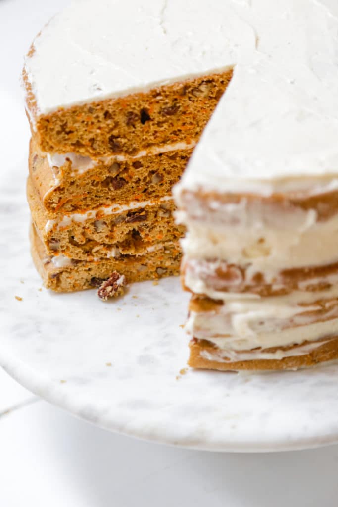 A vegan carrot cake with cream cheese frosting with a piece cut out of it.