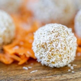 A wooden cake stand with carrot cake balls rolled in shredded coconut and shredded carrots.