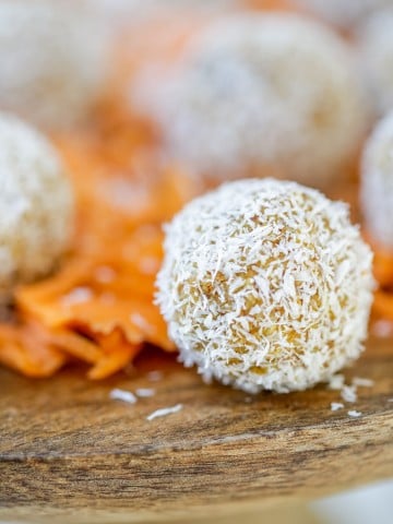 A wooden cake stand with carrot cake balls rolled in shredded coconut and shredded carrots.