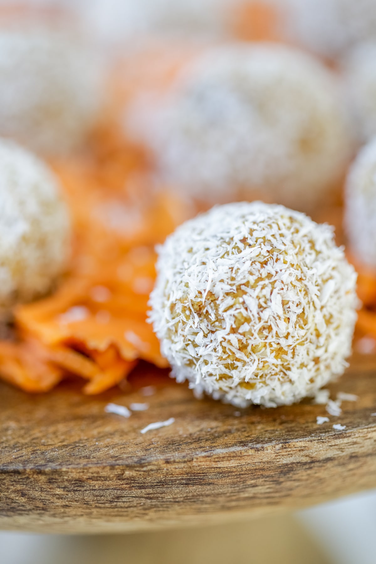 A wooden cake stand with carrot cake balls rolled in shredded coconut and shredded carrots.