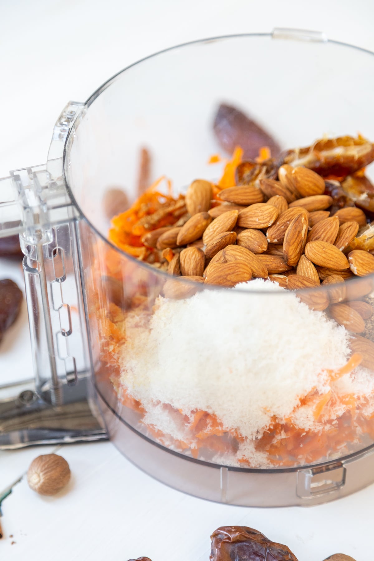 A food processor filled with almonds, dates, shredded coconut and carrots.