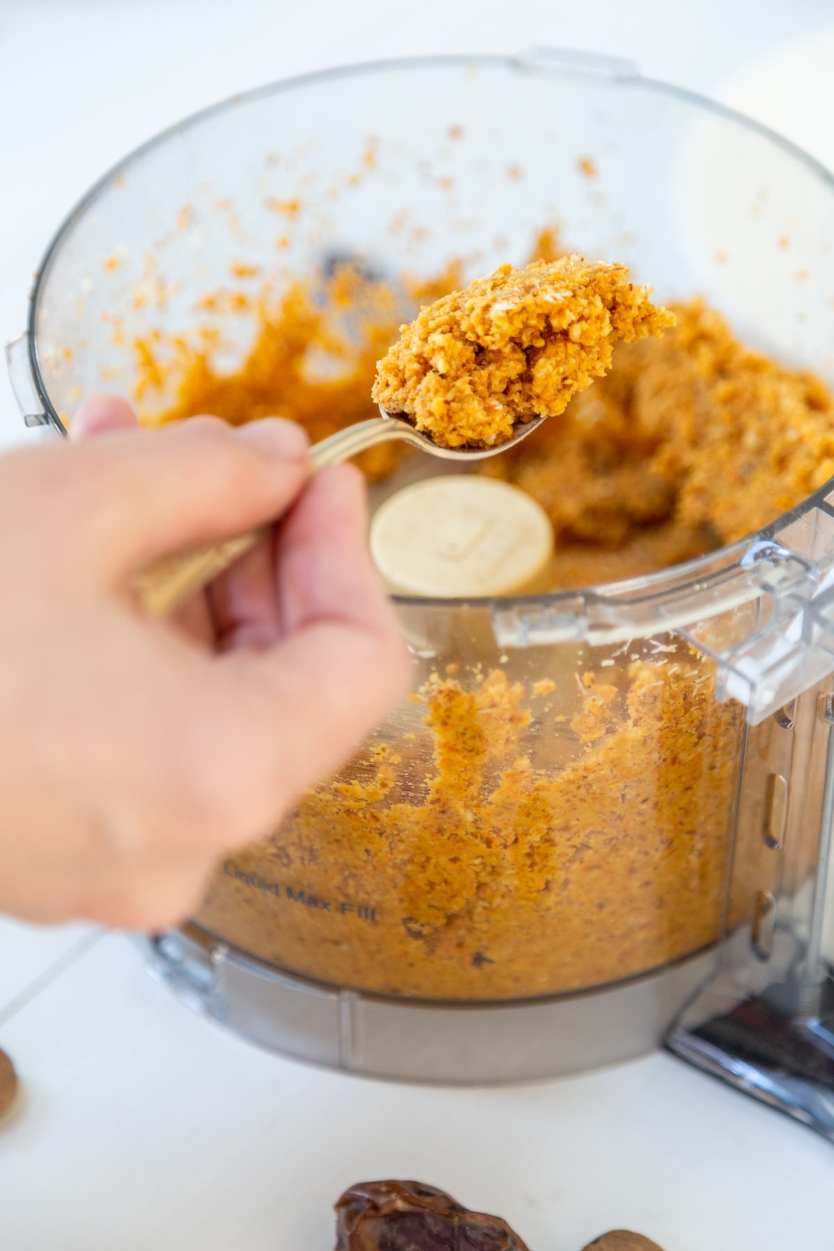 A hand spooning out the batter for carrot bites from a food processor.
