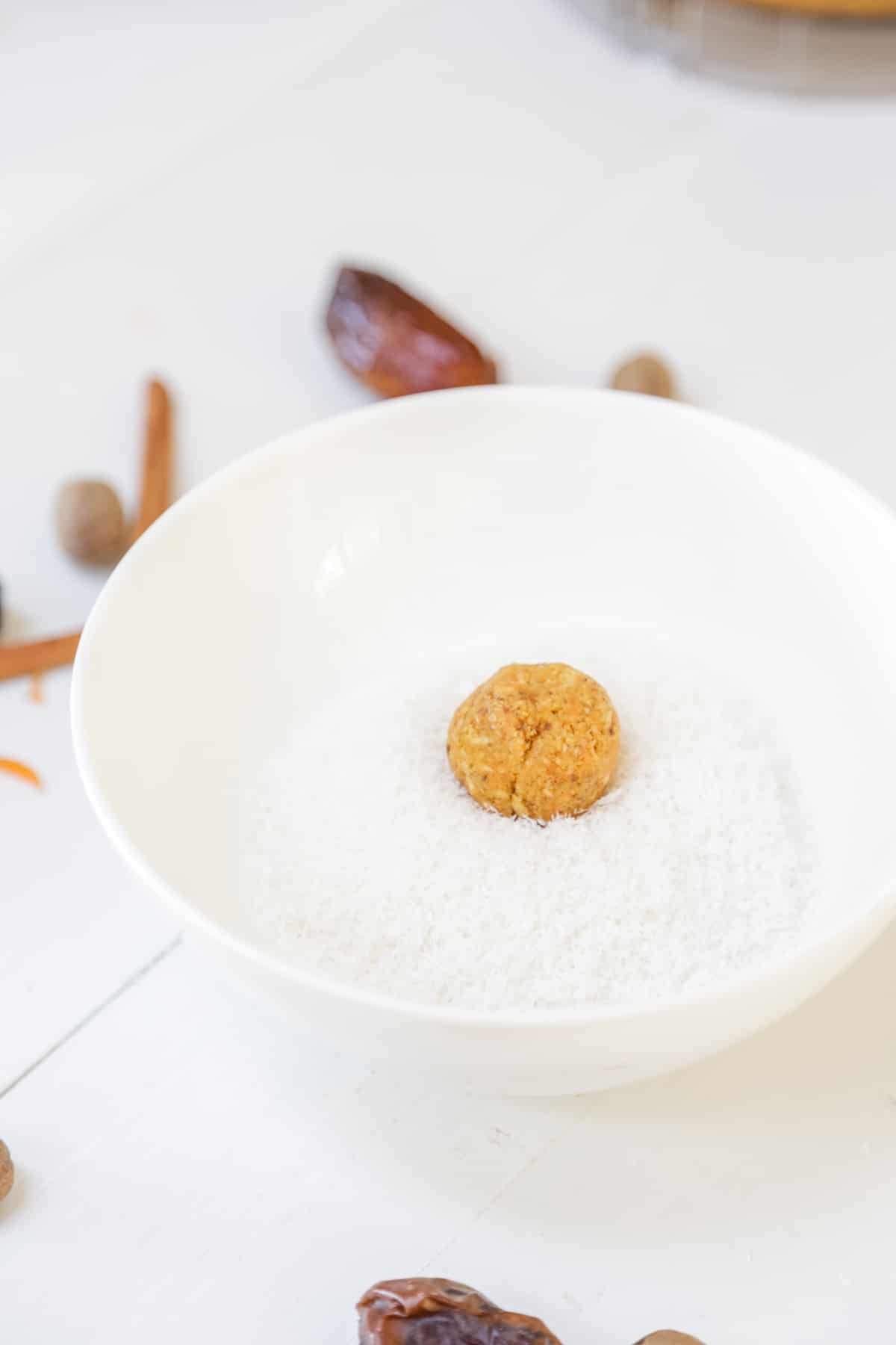 A carrot cake ball in a white bowl with shredded coconut.