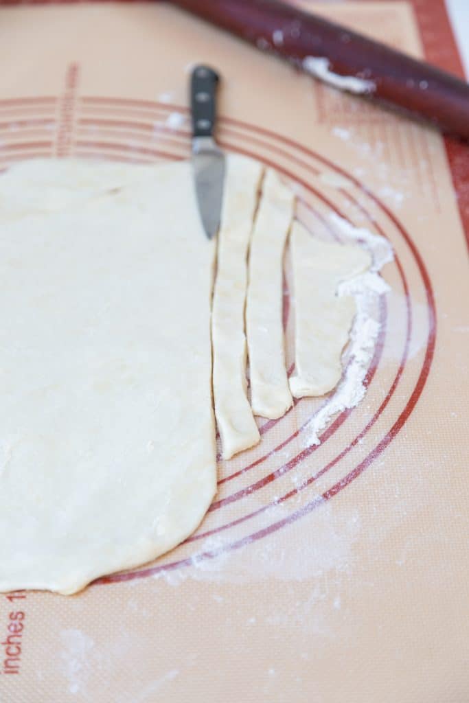 Pie dough rolled out on a silicone mat and strips of dough cut with a knife.