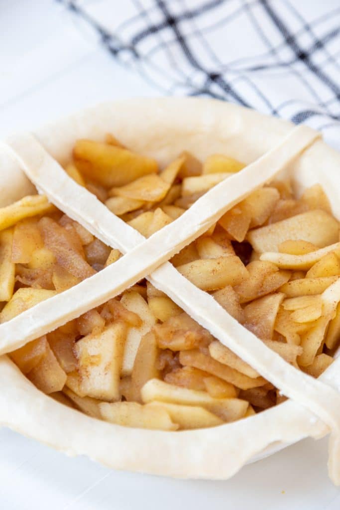 A pie crust filled with apples and 2 strips of dough over the top.