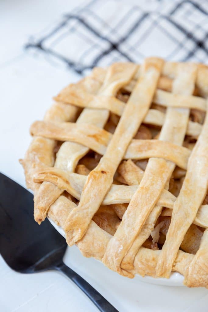 An apple pie with a lattice top and a black pie spatula next to the pie.