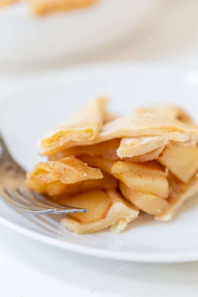 A slice of apple pie with a fork taking a piece of the pie.