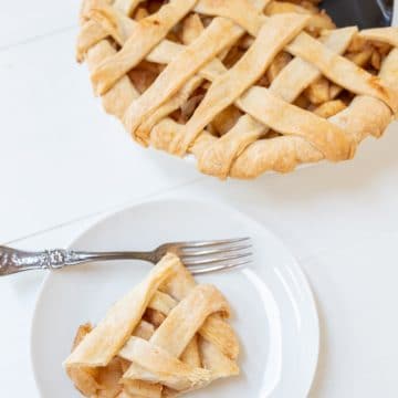 An apple pie with a lattice top and a slice of the pie on a white plate.