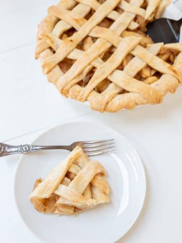 An apple pie with a lattice top and a slice of the pie on a white plate.