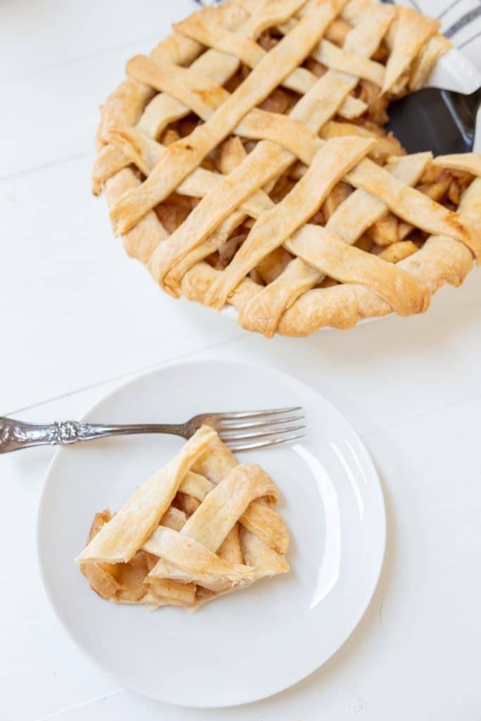 An apple pie with a lattice top and a slice of the pie on a white plate.