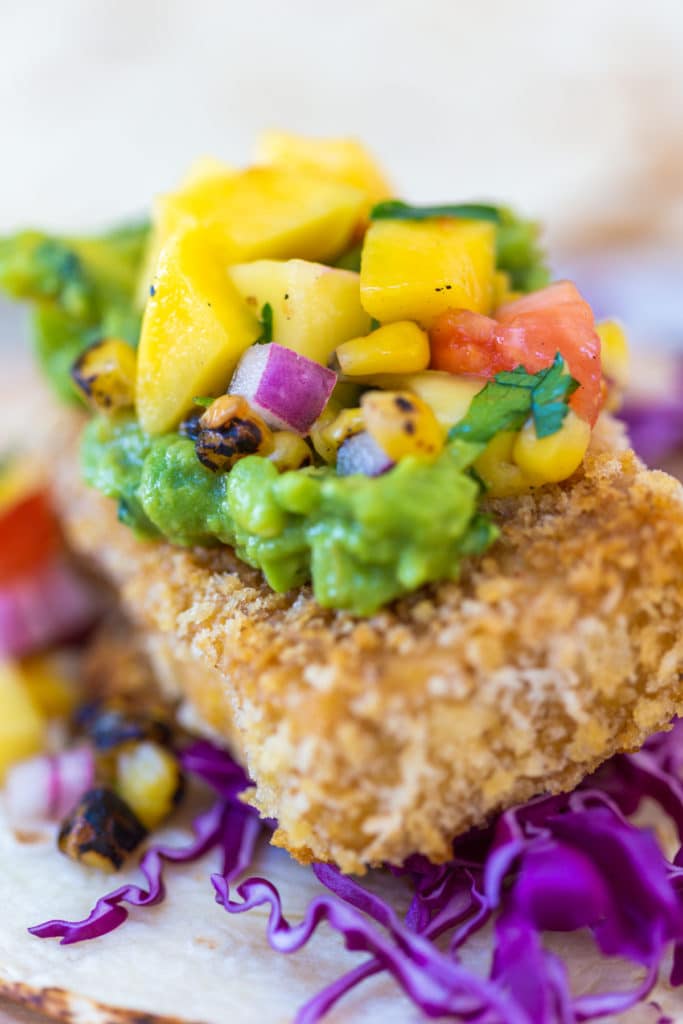 A close-up shot of a breaded tofu taco with avocado and mango salsa.