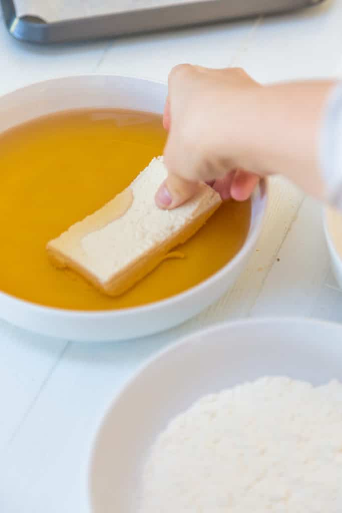 A hand dipping a piece of tofu in a bowl of beer.