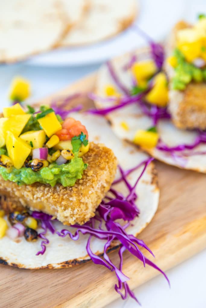 A tortilla with red cabbage, fried breaded tofu, mashed avocado, and mango salsa.