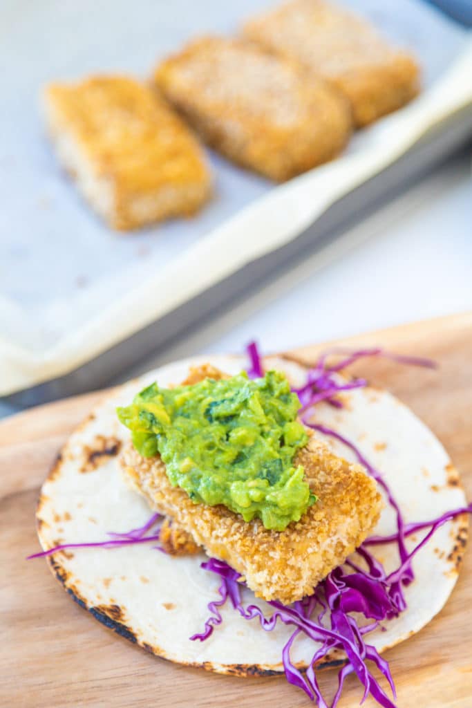 A tortilla with shredded cabbage, a breaded fried tofu stick, and mashed avocado.