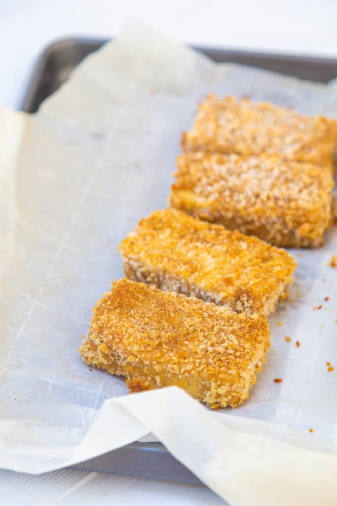 Deep fried pieces of tofu on a parchment lined baking sheet.