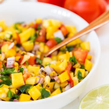 A white bowl with mango salsa and a gold spoon in the bowl.